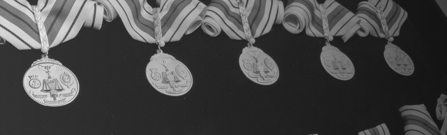 Imagem de fundo mostrando foto preto e branco com Medalhas da Ordem do Mérito Judiciário penduradas lado a lado, representando honra, excelência e dedicação.