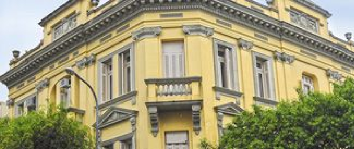 Fachada da 3ª Circunscrição Judiciária Militar, em Porto Alegre. Prédio histórico de três andares, pintado de amarelo com detalhes em cinza. O edifício tem janelas altas, sacadas com guarda-corpo e detalhes arquitetônicos clássicos. Árvores parcialmente encobrem a base da construção.