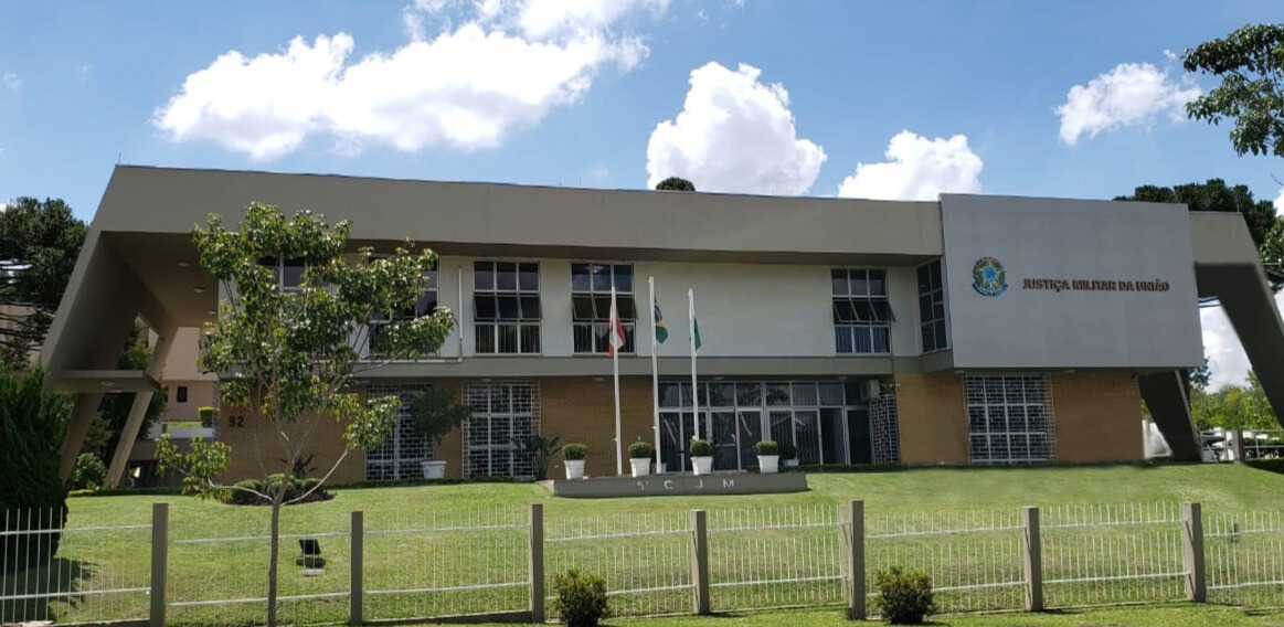 Fachada da 5ª CJM, com jurisdição no Paraná e Santa Catarina. Prédio de dois andares com gramado, fachada em tons terrosos e três bandeiras hasteadas. Há uma cobertura inclinada sobre a entrada.